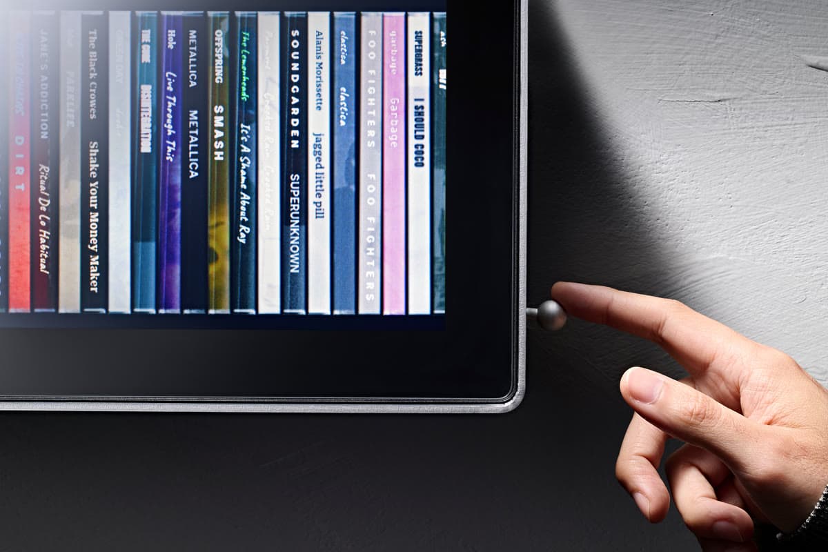 A finger reaching for the small round switch on the side of Spine, with album spines lit on the display.