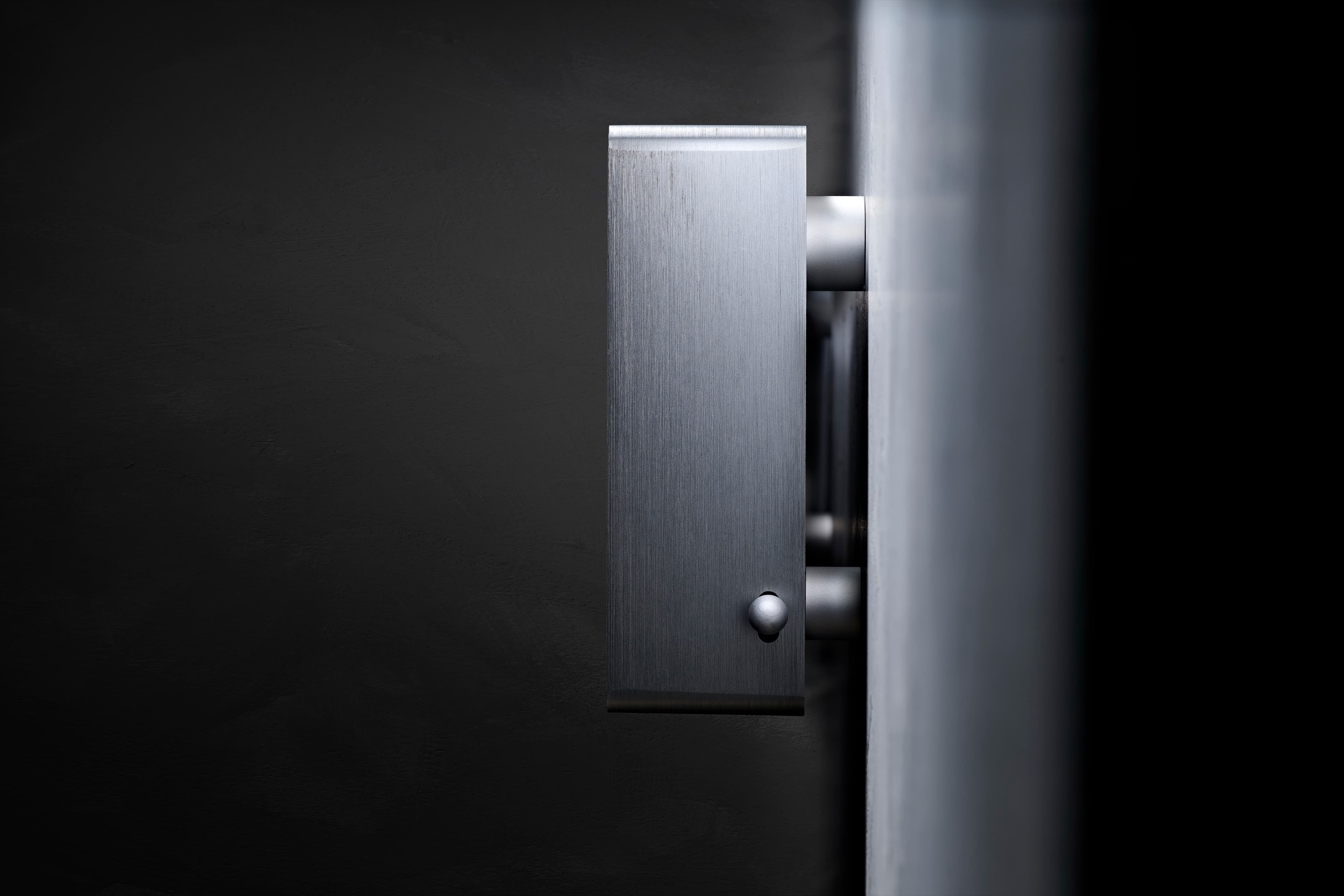 Spine seen side-on against a dark wall, showing the brushed aluminium end, the side switch and the wall mount
